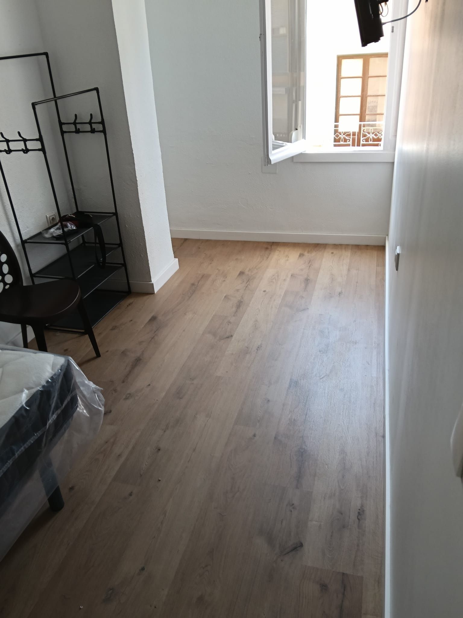 Habitación vacía con suelo de madera clara, paredes blancas y una ventana por la que entra la luz del día.