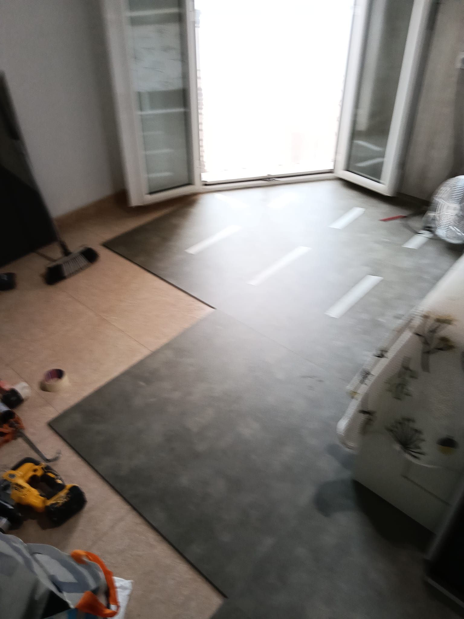 Habitación parcialmente vacía, con suelo gris, puertas abiertas y herramientas esparcidas sobre una zona cubierta de cartón.