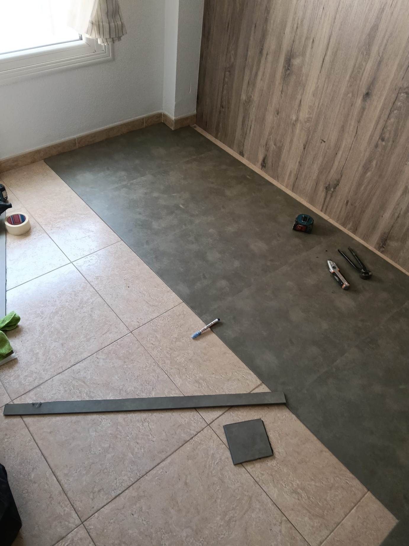 Suelo parcialmente embaldosado con una capa base verde y paneles de madera en las paredes de una habitación en renovación