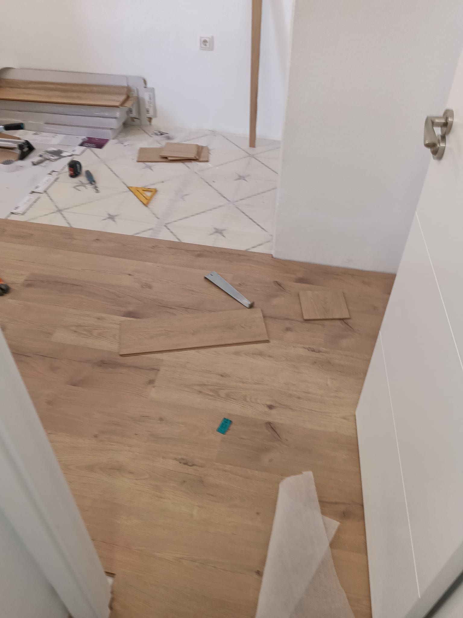 Pasillo parcialmente renovado, con suelo de madera, herramientas esparcidas y restos de azulejos al fondo