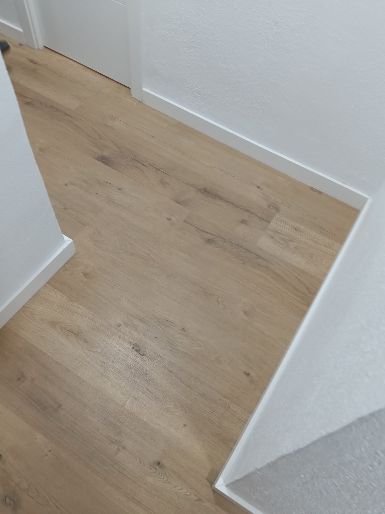 Rincón de un pasillo estrecho con suelo de madera clara y paredes y molduras blancas