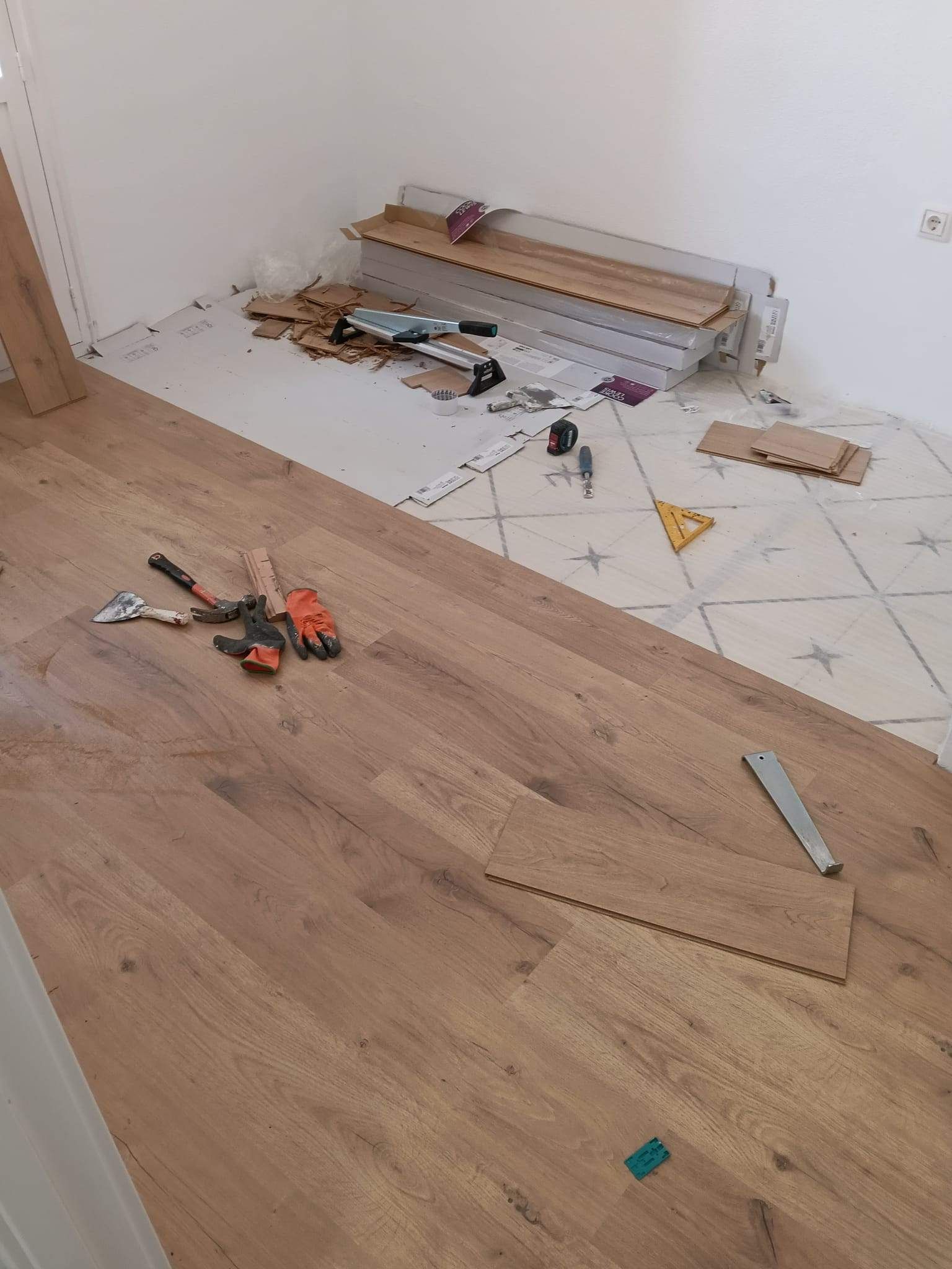 Caja de herramientas y herramientas dispersas sobre un suelo de madera, junto a una pared en construcción.