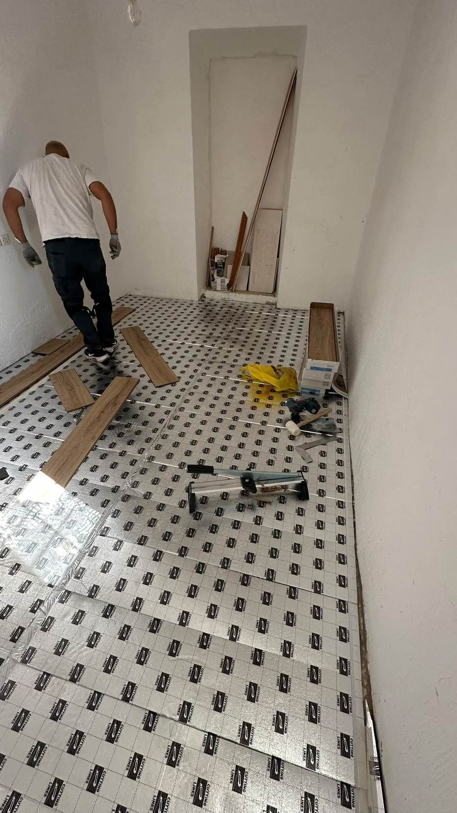 Trabajador instalando el suelo en una habitación, con herramientas y paneles en el suelo