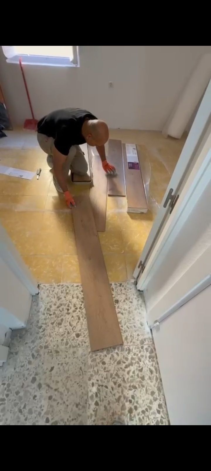 Persona arrodillada en el suelo de un pasillo, colocando cajas junto a una puerta y una ventana.