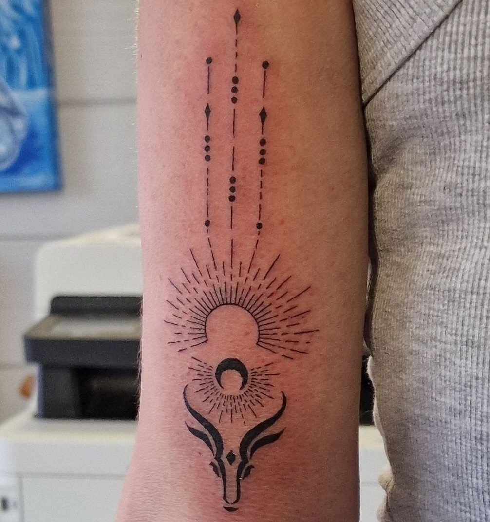 Tatouage d'une tête de taureau avec un motif de soleil rayonnant et des lignes perlées.