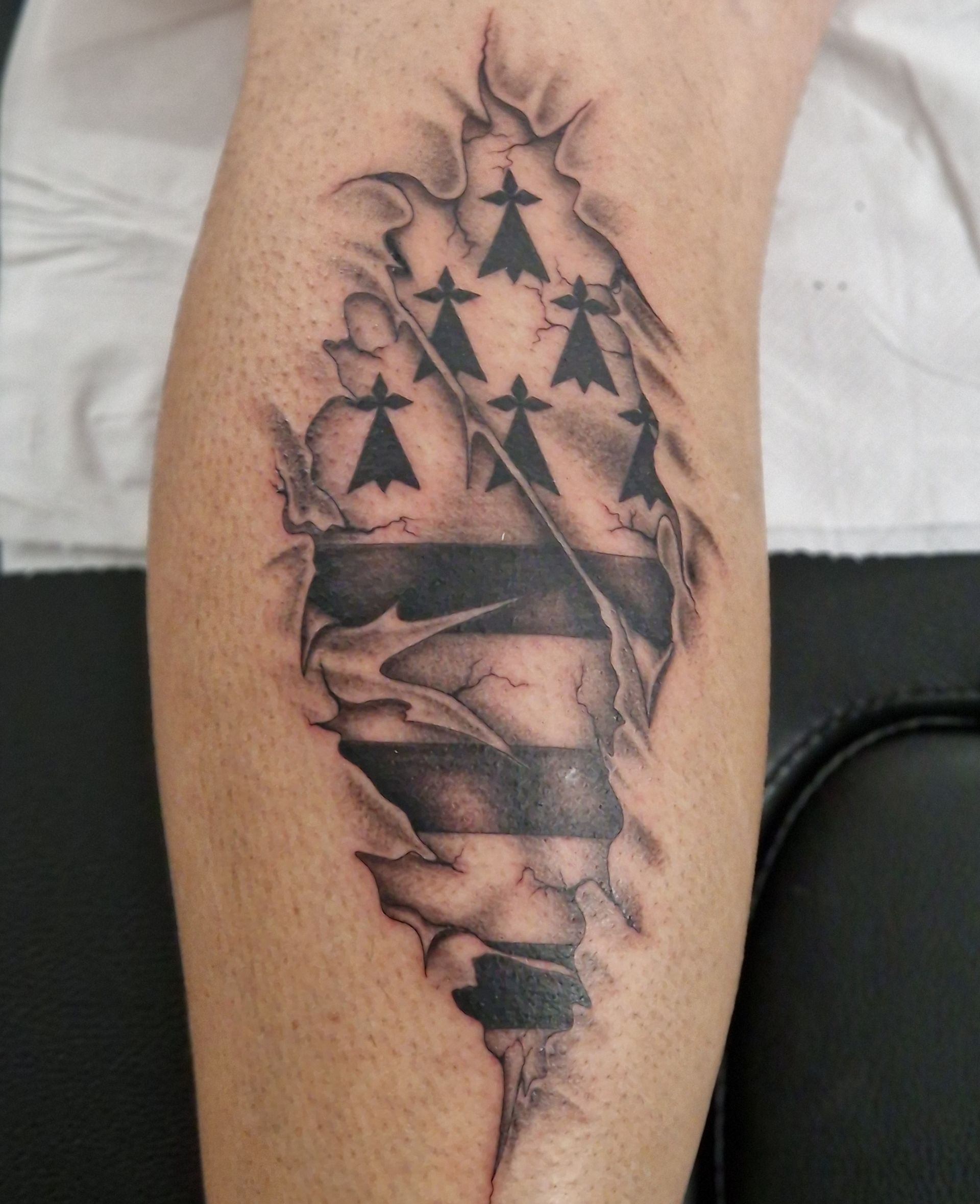 Tatouage effet peau déchirée révélant le drapeau noir et blanc de la Bretagne.