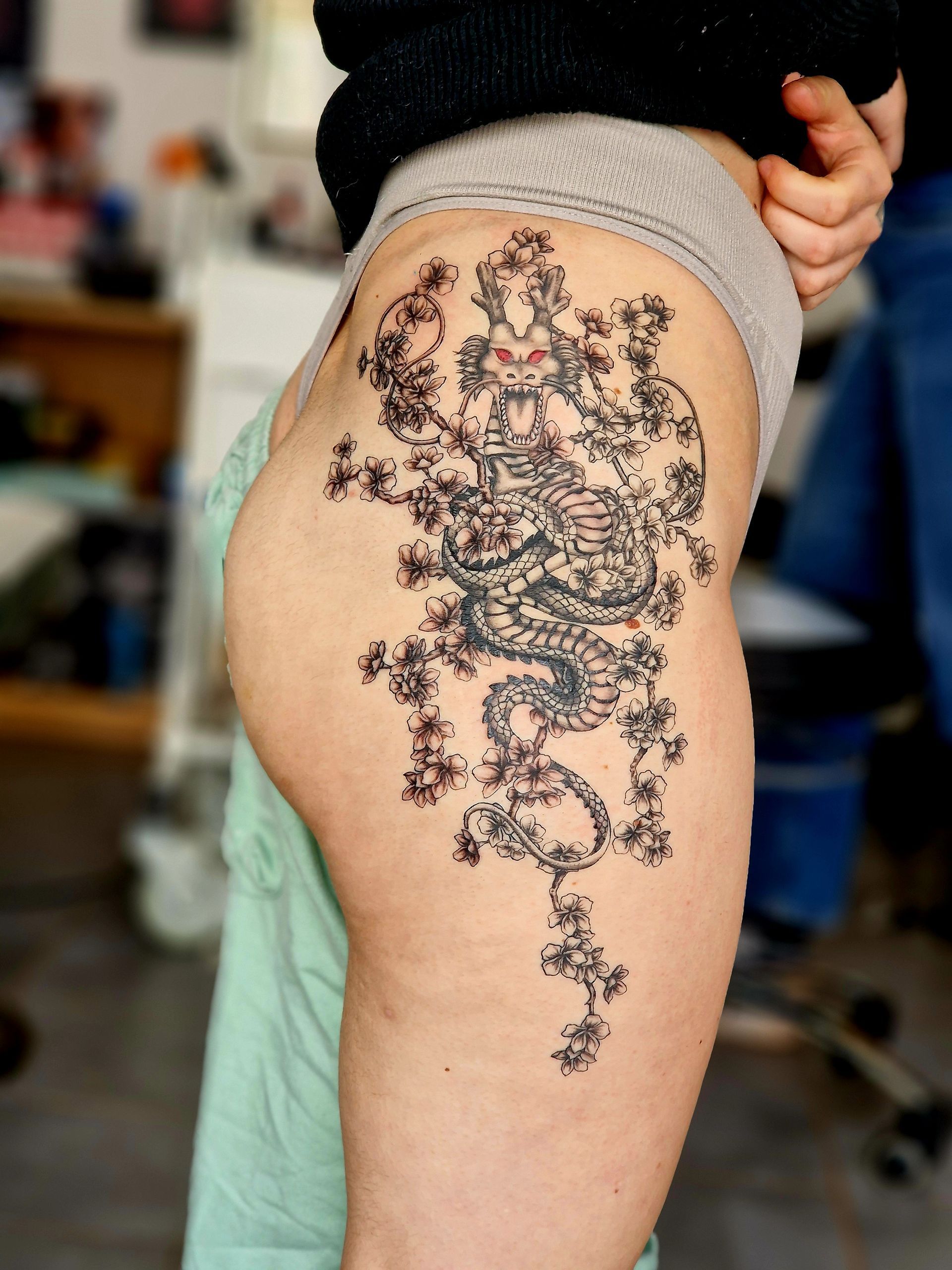 Tatouage représentant un dragon détaillé et un motif floral sur la hanche. 