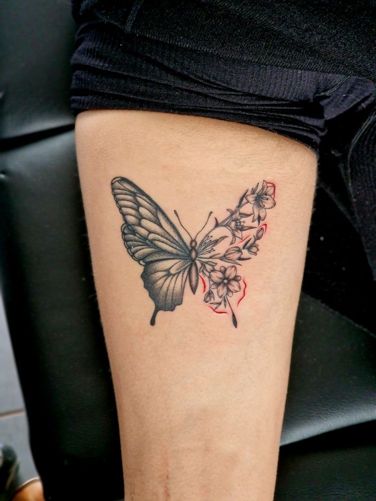 Tatouage d'un papillon sur le bras, un côté détaillé, l'autre floral avec un contour rouge.