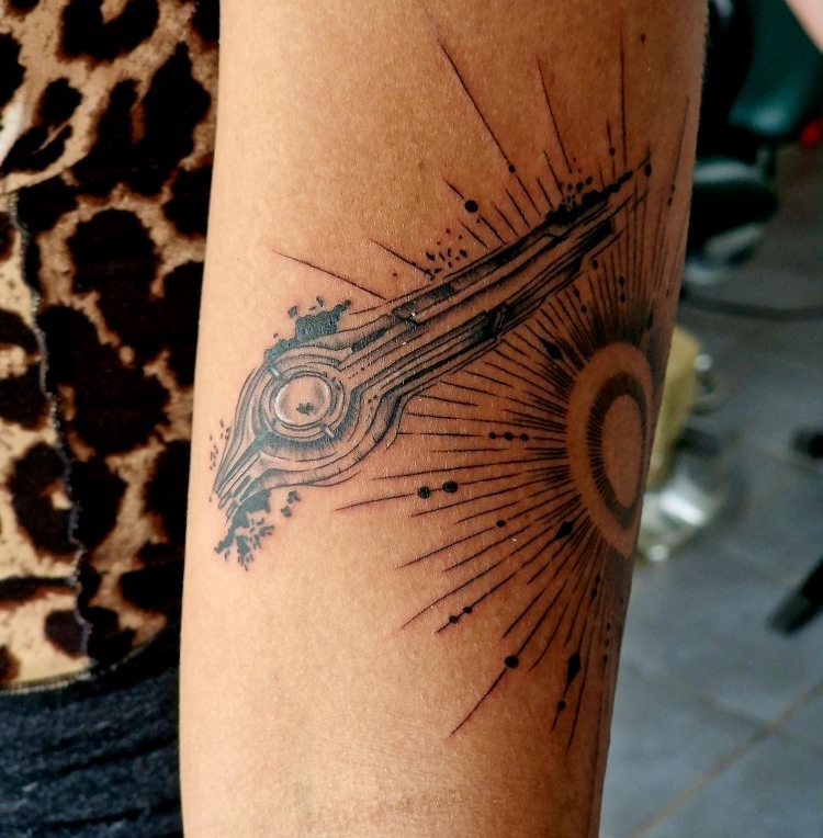 Tatouage représentant une clé abstraite aux lignes rayonnantes, ressemblant à un soleil, sur le bras d'une personne.