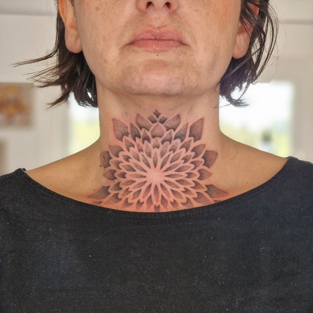 Femme avec un tatouage floral noir et gris détaillé sur le cou.