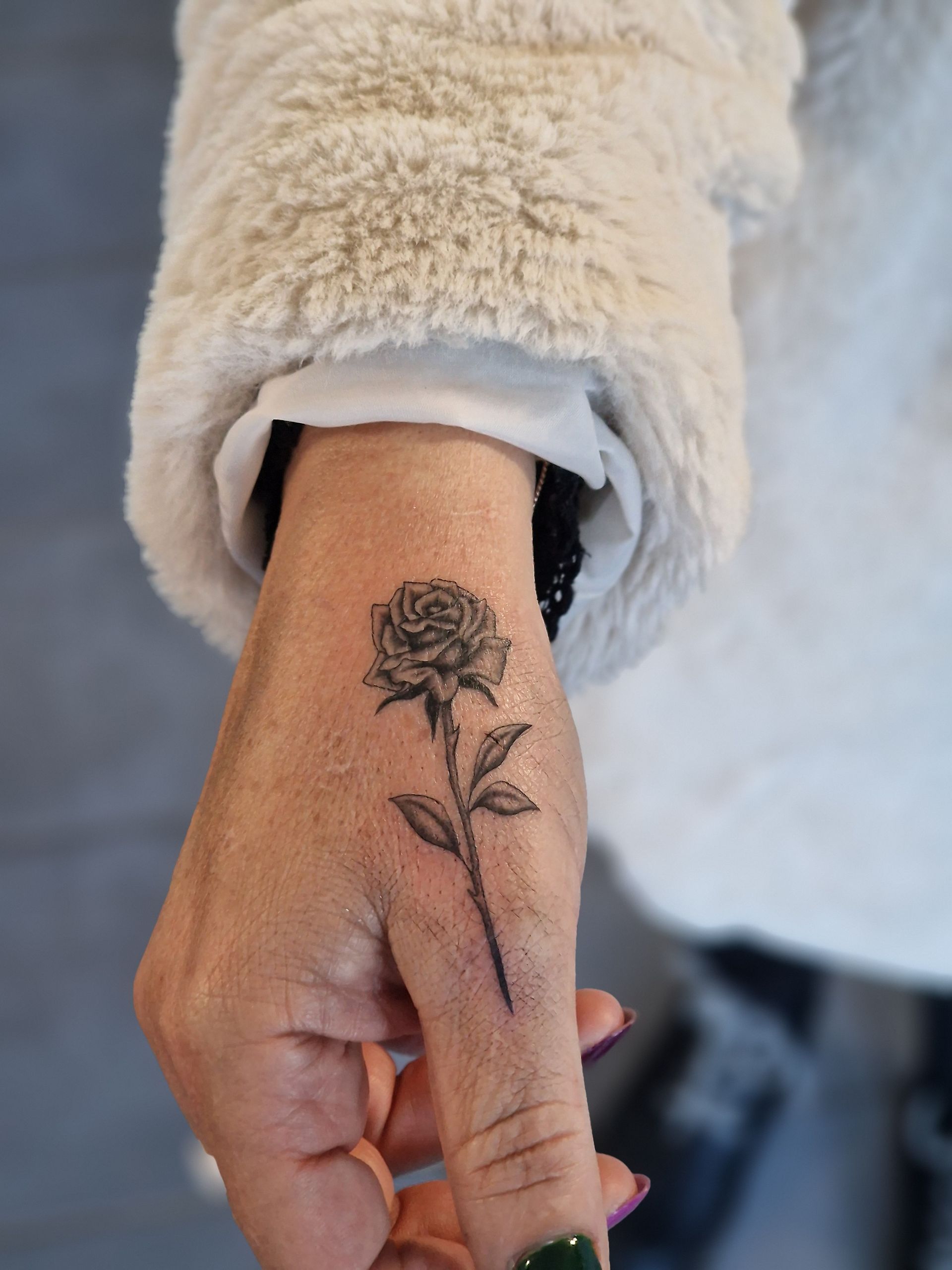 Main ornée d'un petit tatouage de rose. 