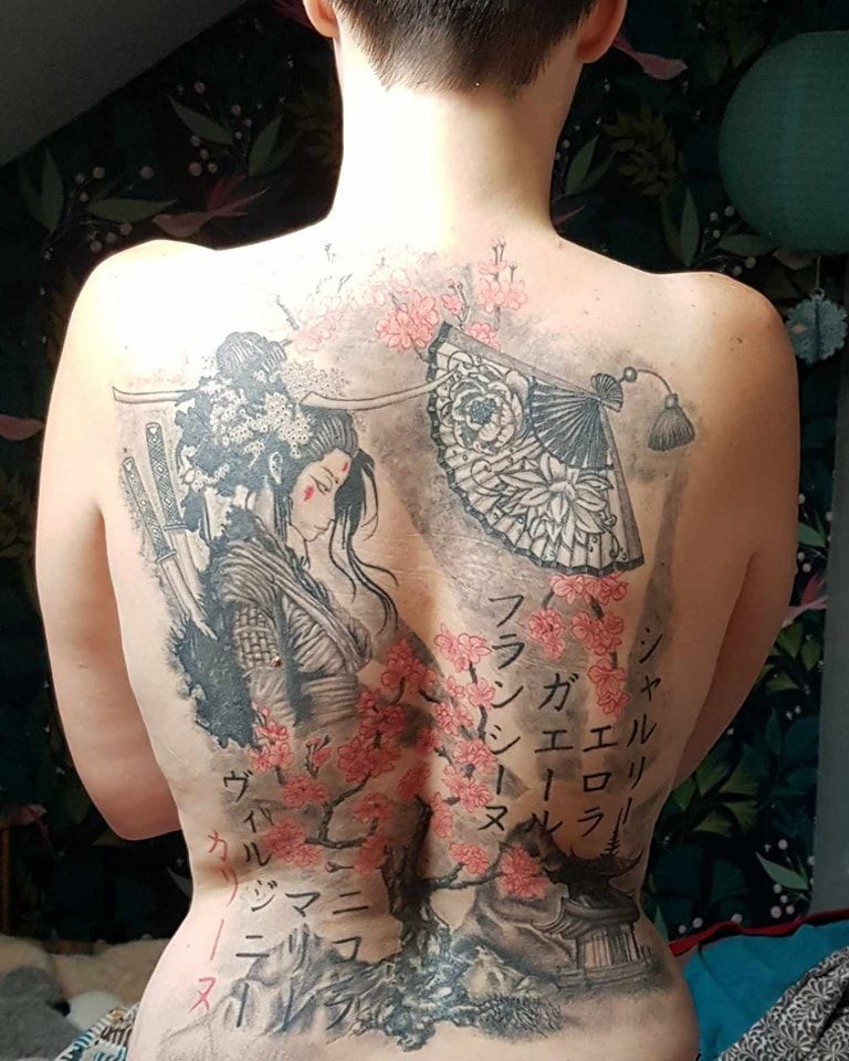 Tatouage dans le dos d'une geisha avec texte japonais, éventail et fleurs de cerisier en noir et rouge.