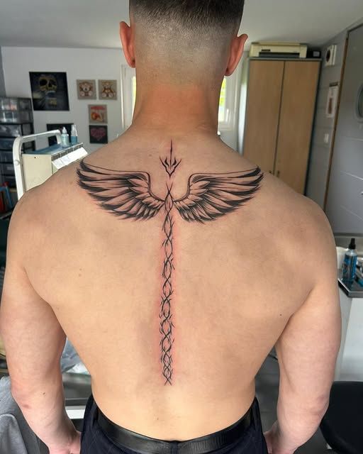 Dos d'une personne avec un tatouage d'ailes et un motif central sur la colonne vertébrale.