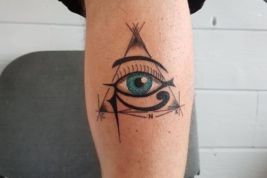 Tatouage d'un œil inscrit dans un triangle. L'œil est turquoise avec un contour et des détails noirs, sur une jambe.