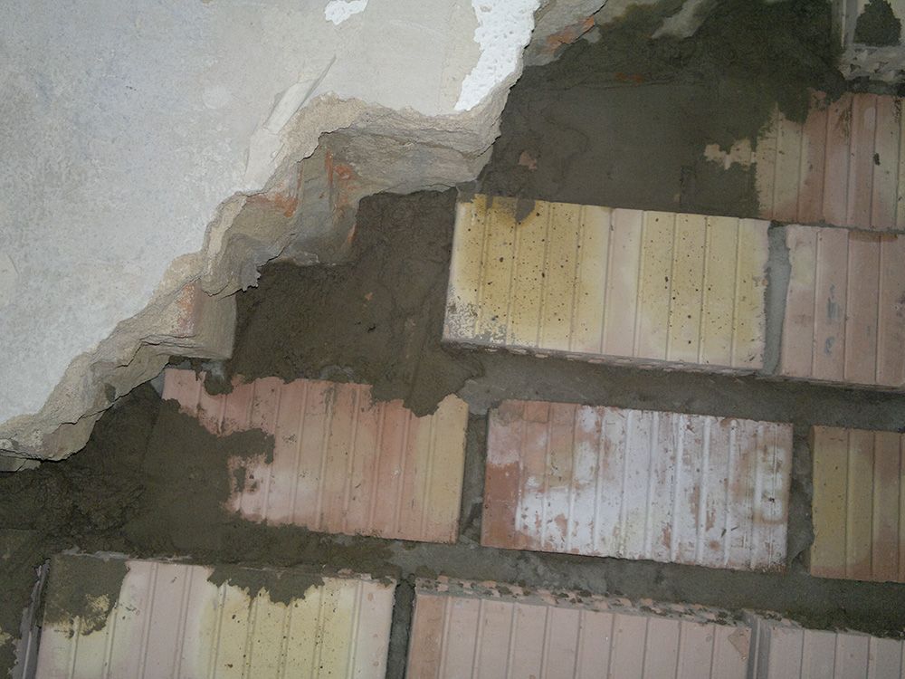 Eine Nahaufnahme einer Ziegelwand, auf die Beton aufgetragen wird.