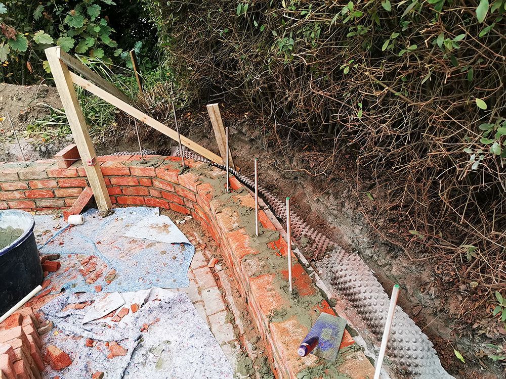 Neben einem Holzzaun wird eine Ziegelmauer gebaut.
