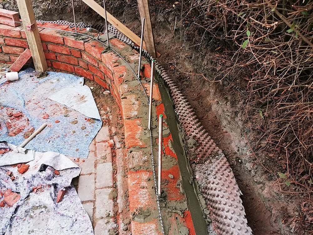 In einem Loch im Boden wird eine Ziegelmauer gebaut.