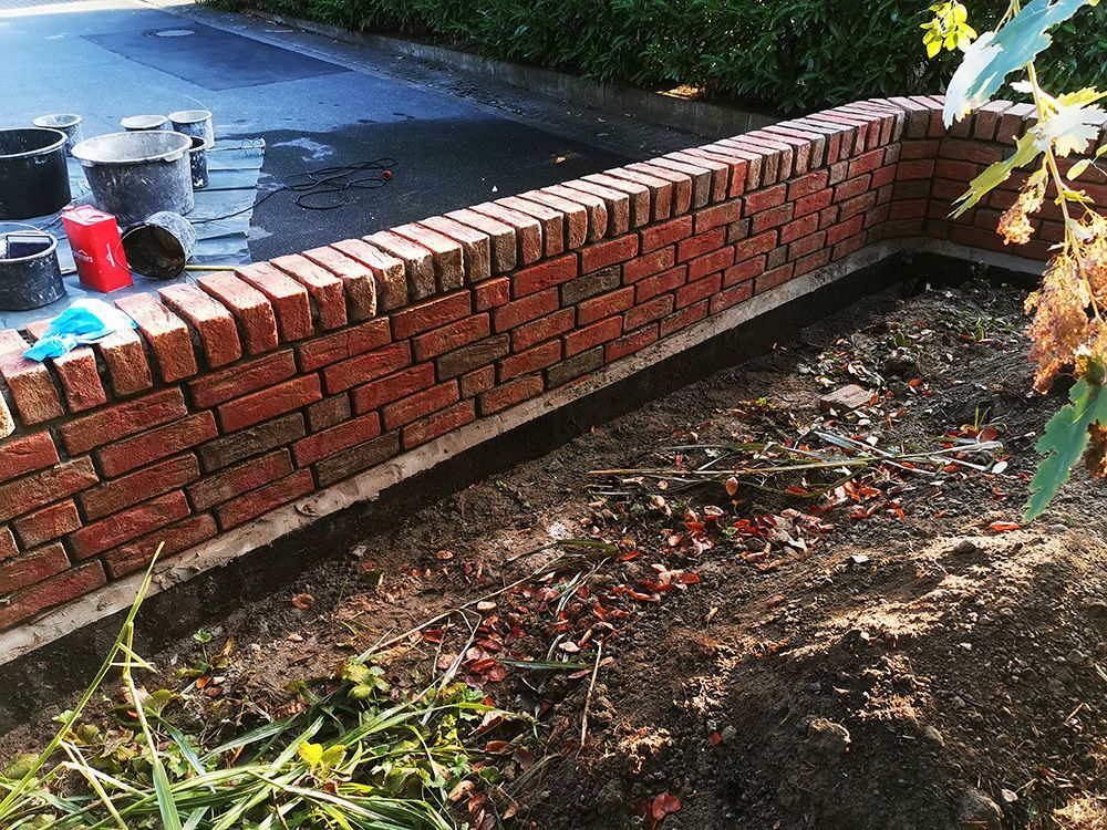 Neben einer Straße wird eine Backsteinmauer gebaut.