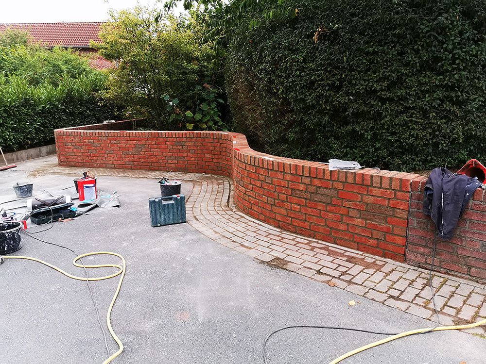 In einer Einfahrt wird eine Backsteinmauer gebaut.