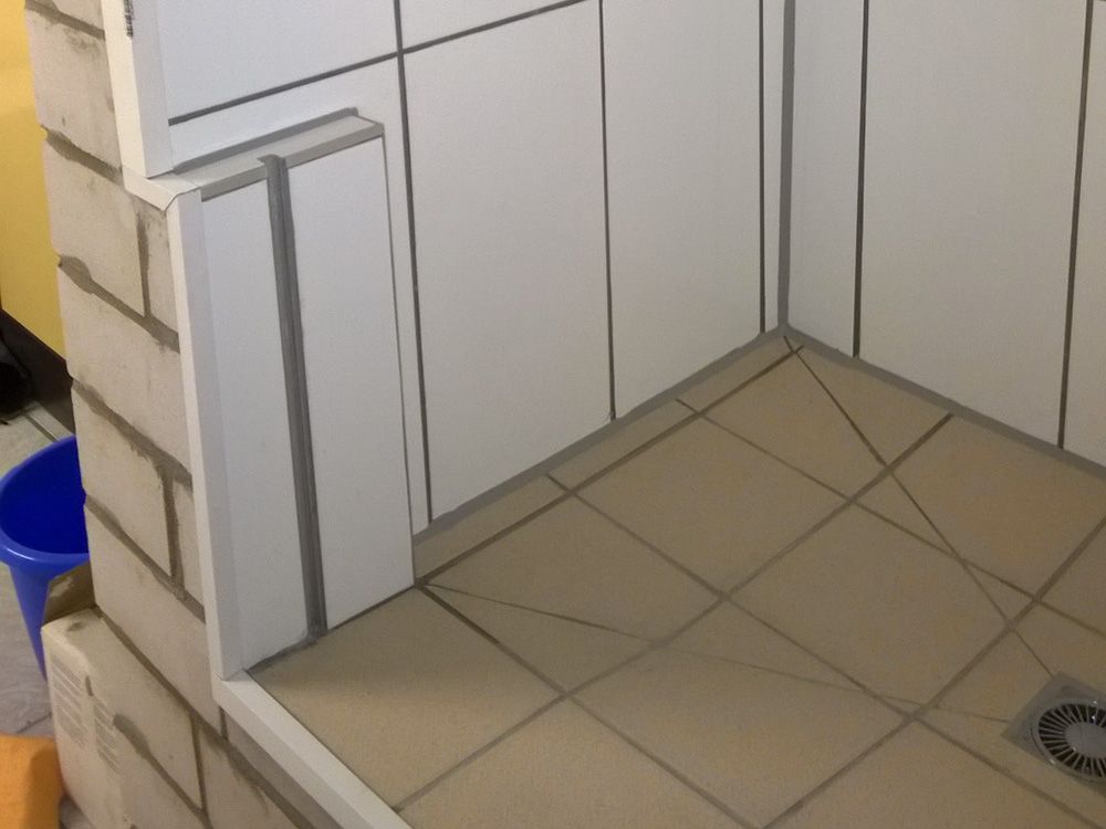 Eine Badezimmerecke mit weißen Fliesen und einem blauen Eimer