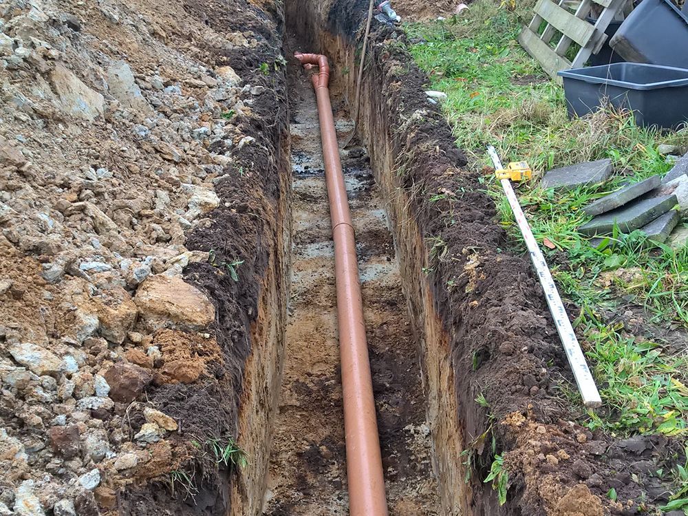 In einem Graben im Erdreich wird ein Rohr verlegt.