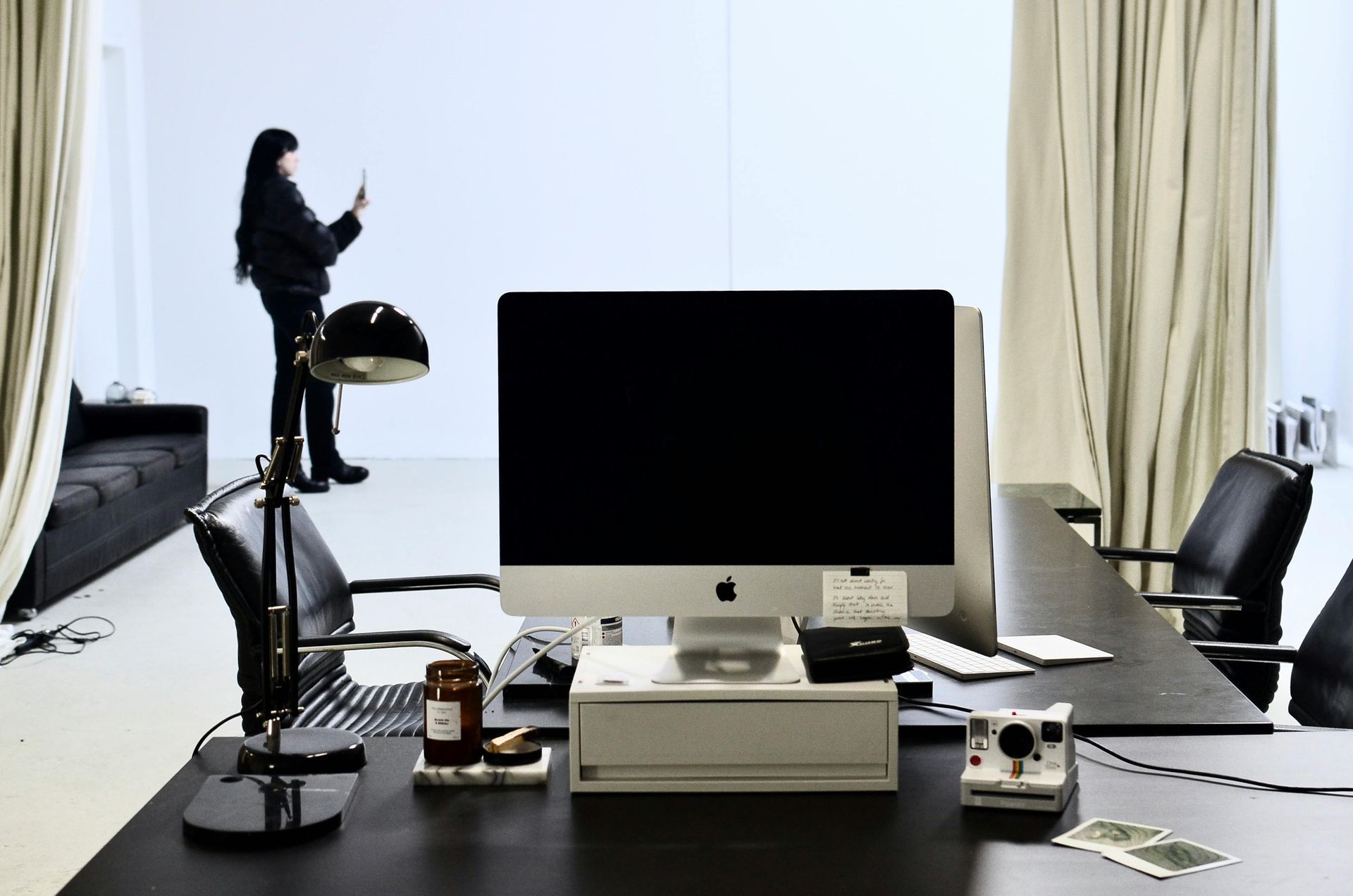 Intérieur de bureau avec une personne prenant une photo ; bureau avec ordinateur, lampe et accessoires.
