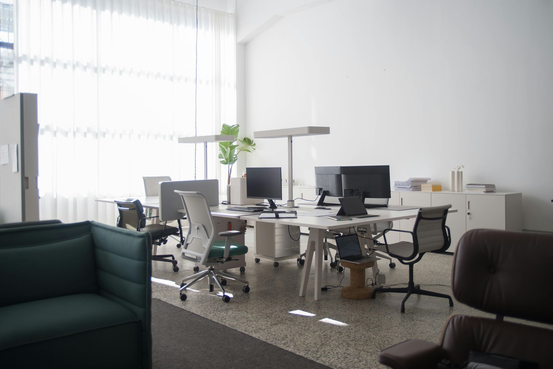 Espace de bureau lumineux et vide, avec bureaux, chaises et écrans ; un canapé vert au premier plan.