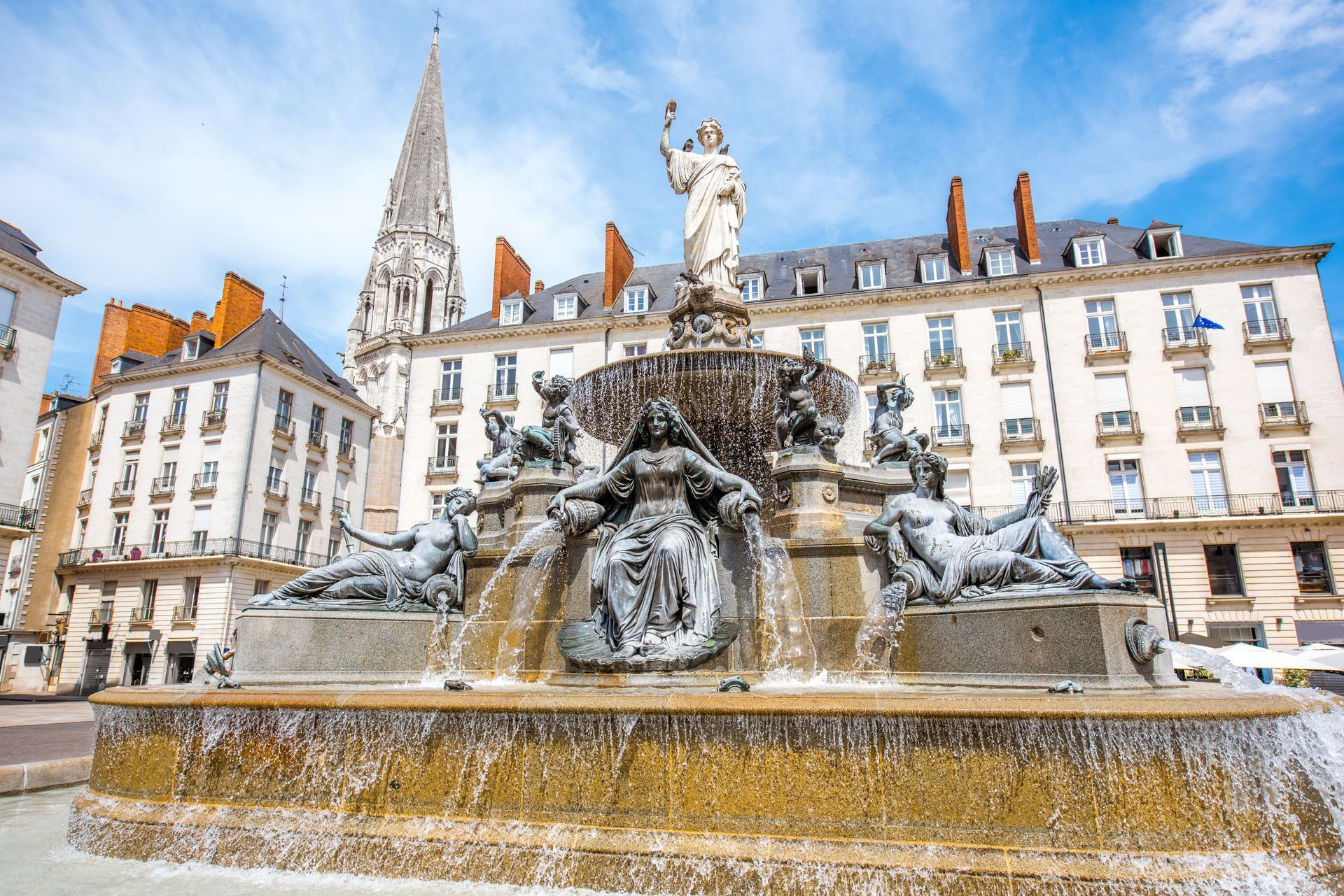 La fontaine de Neptune à Nantes, en France, avec son eau en cascade, ses statues et un immeuble à haute flèche en arrière-plan.