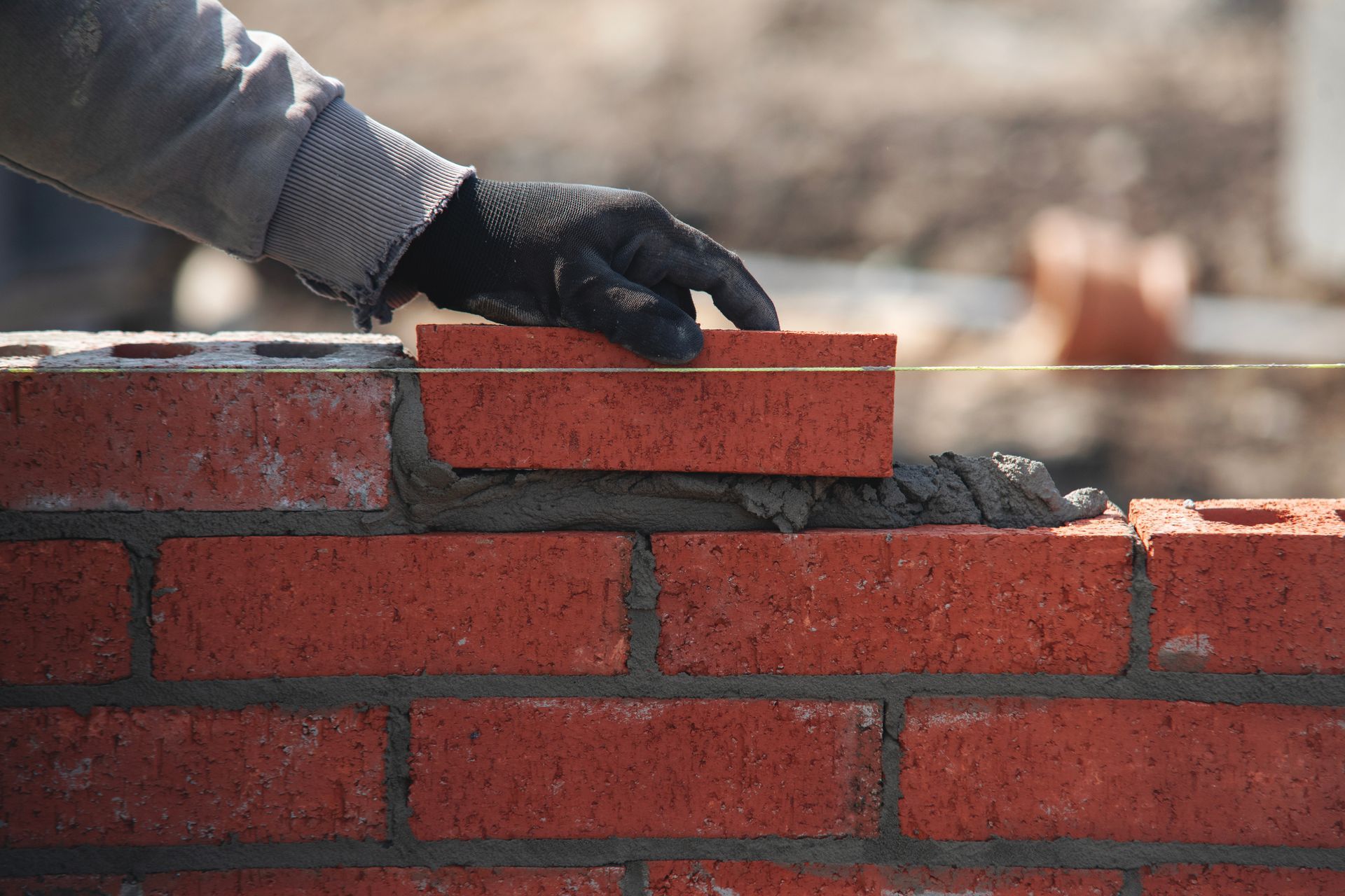 Une main gantée de noir pose une brique sur un lit de mortier, faisant partie d'un mur de briques en construction.