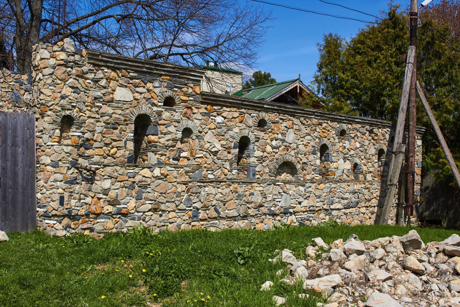 Mur en pierre percé d'ouvertures cintrées, toit vert visible derrière.