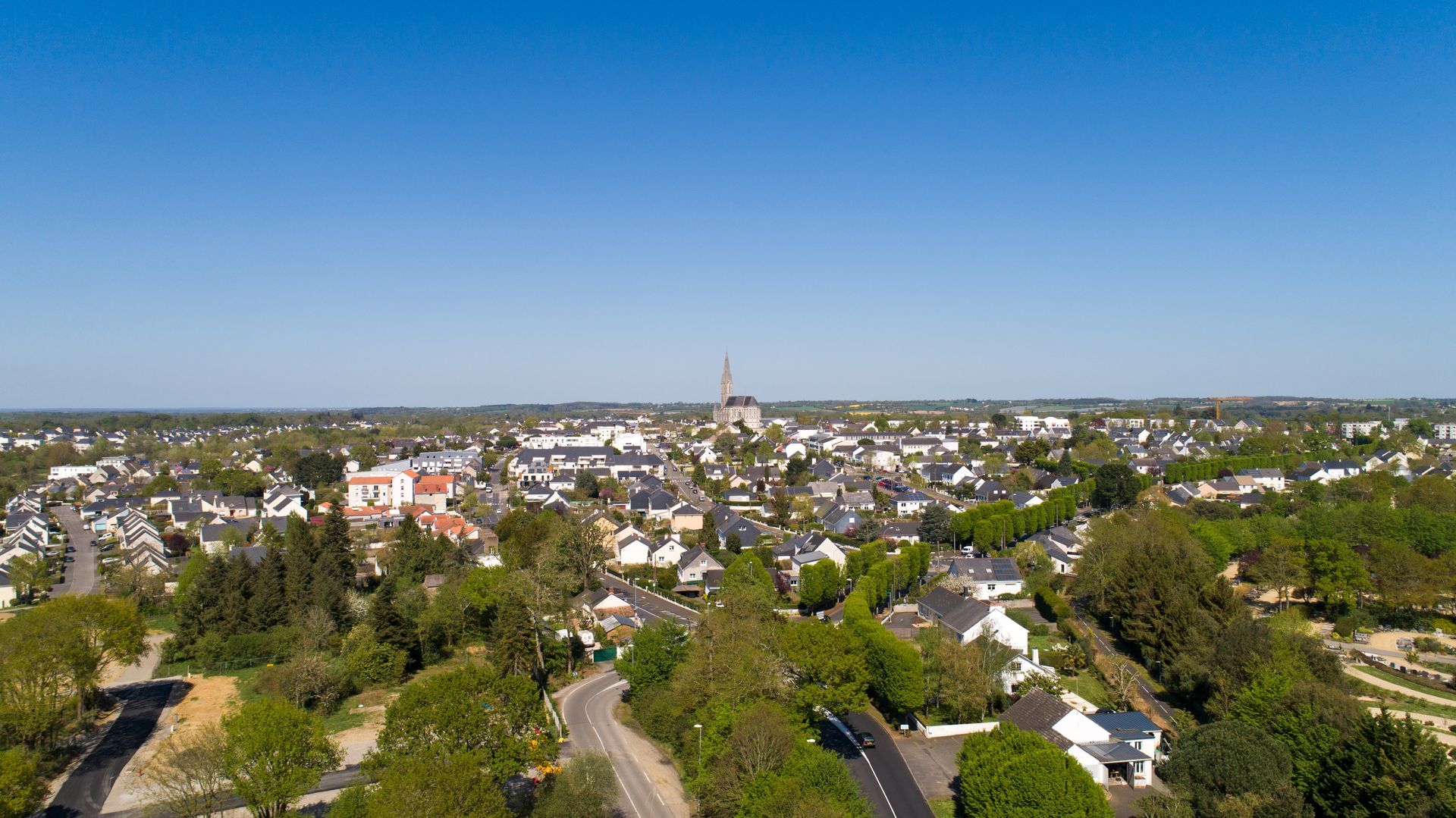 Vue aérienne d'une ville avec un haut clocher d'église, des arbres verts et un ciel bleu.