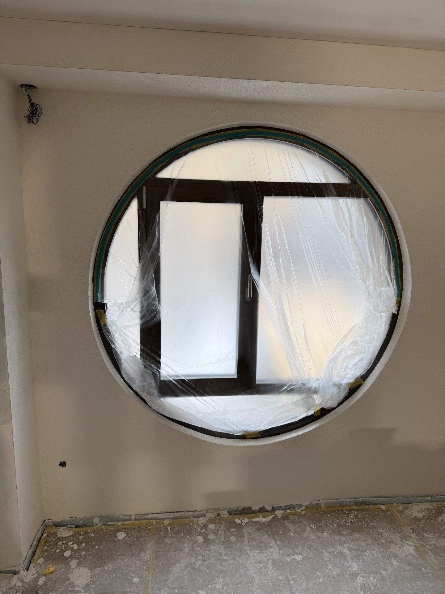 Leerer Raum mit einem runden Fenster und einer schwarz umrandeten Öffnung, die mit durchscheinendem Kunststoff abgedeckt ist.