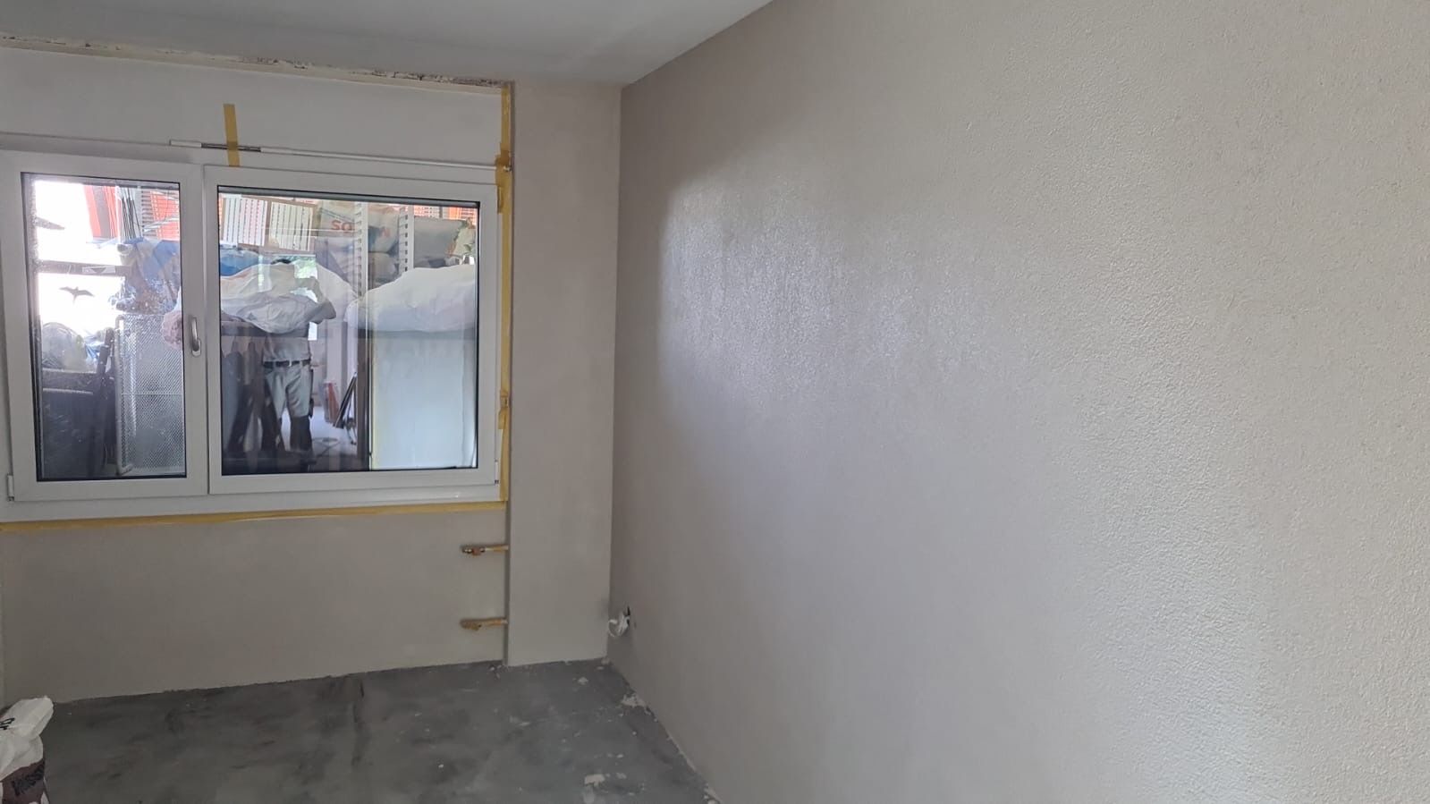 Leeres beigefarbenes Zimmer mit Fenster und nacktem grauen Boden.