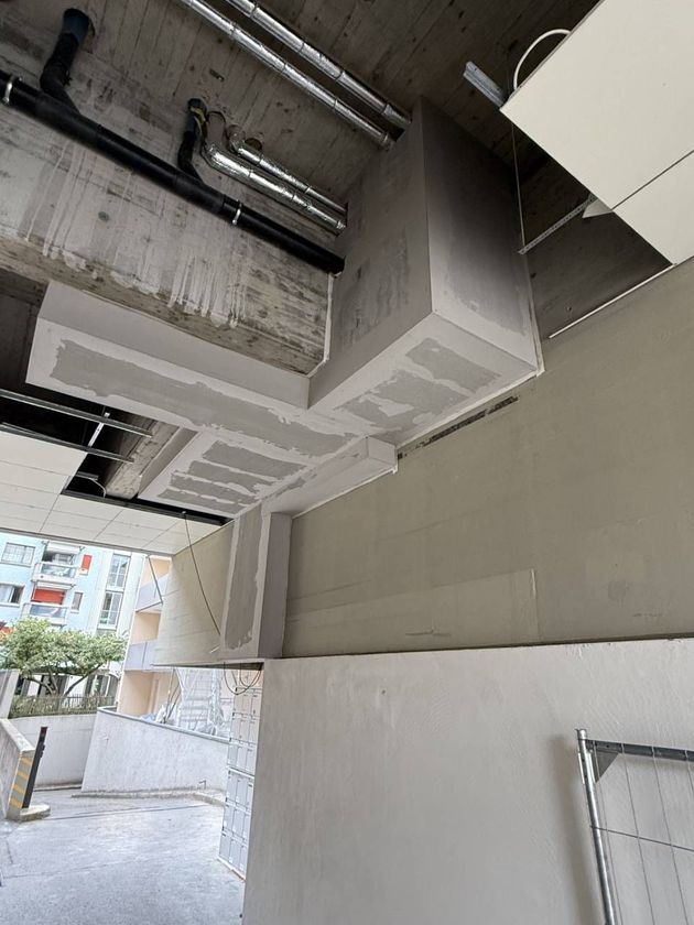 Unterseite eines Gebäudevordachs mit freiliegenden Leitungen, Betonbalken und grauen Wänden in der Nähe eines Gehwegs