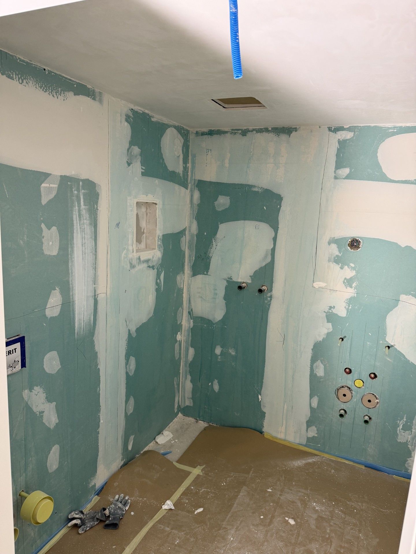 Kleines Badezimmer im Umbau mit ausgebesserten Trockenbauwänden, blauen Wänden und Werkzeug auf dem Boden.
