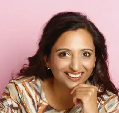 A woman in a striped shirt is smiling with her hand on her chin.