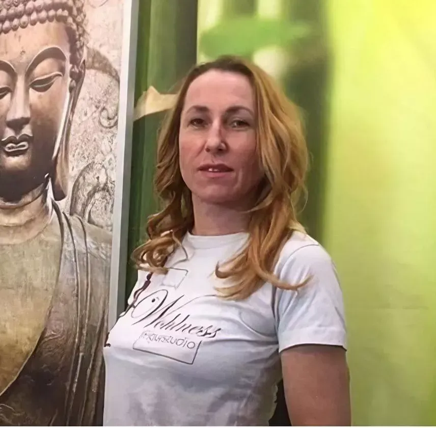 Frau in weißem T-Shirt steht neben einem Buddha-Wandbild und einer grünen Wand