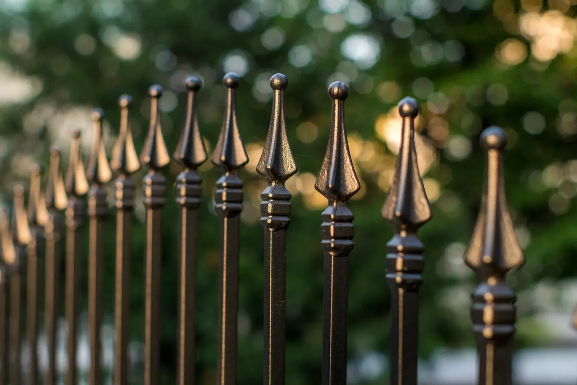 Eine Nahaufnahme eines schmiedeeisernen Zauns mit Bäumen im Hintergrund.