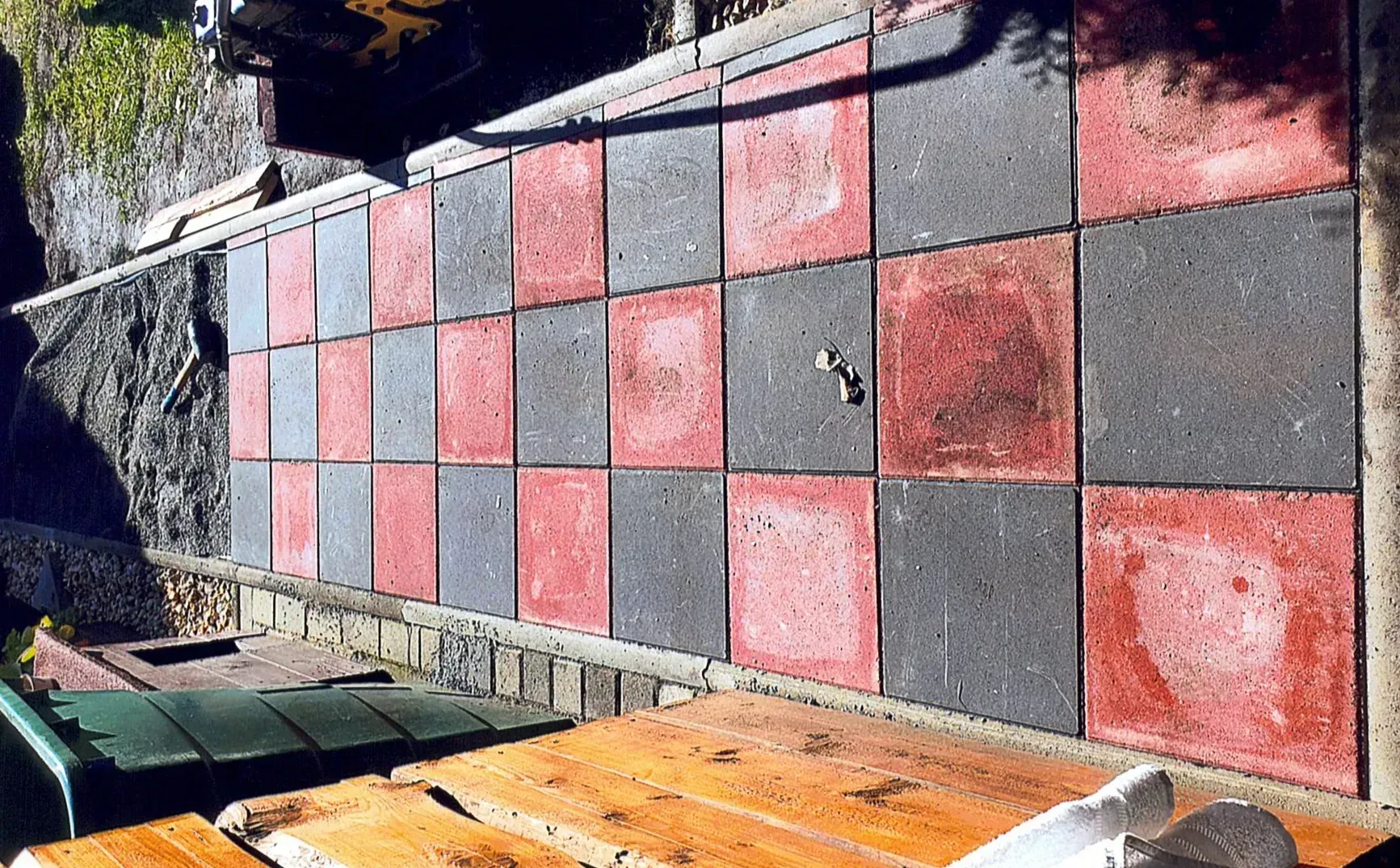 Ein Gehweg aus rot-schwarz karierten Fliesen und einem Holztisch davor.