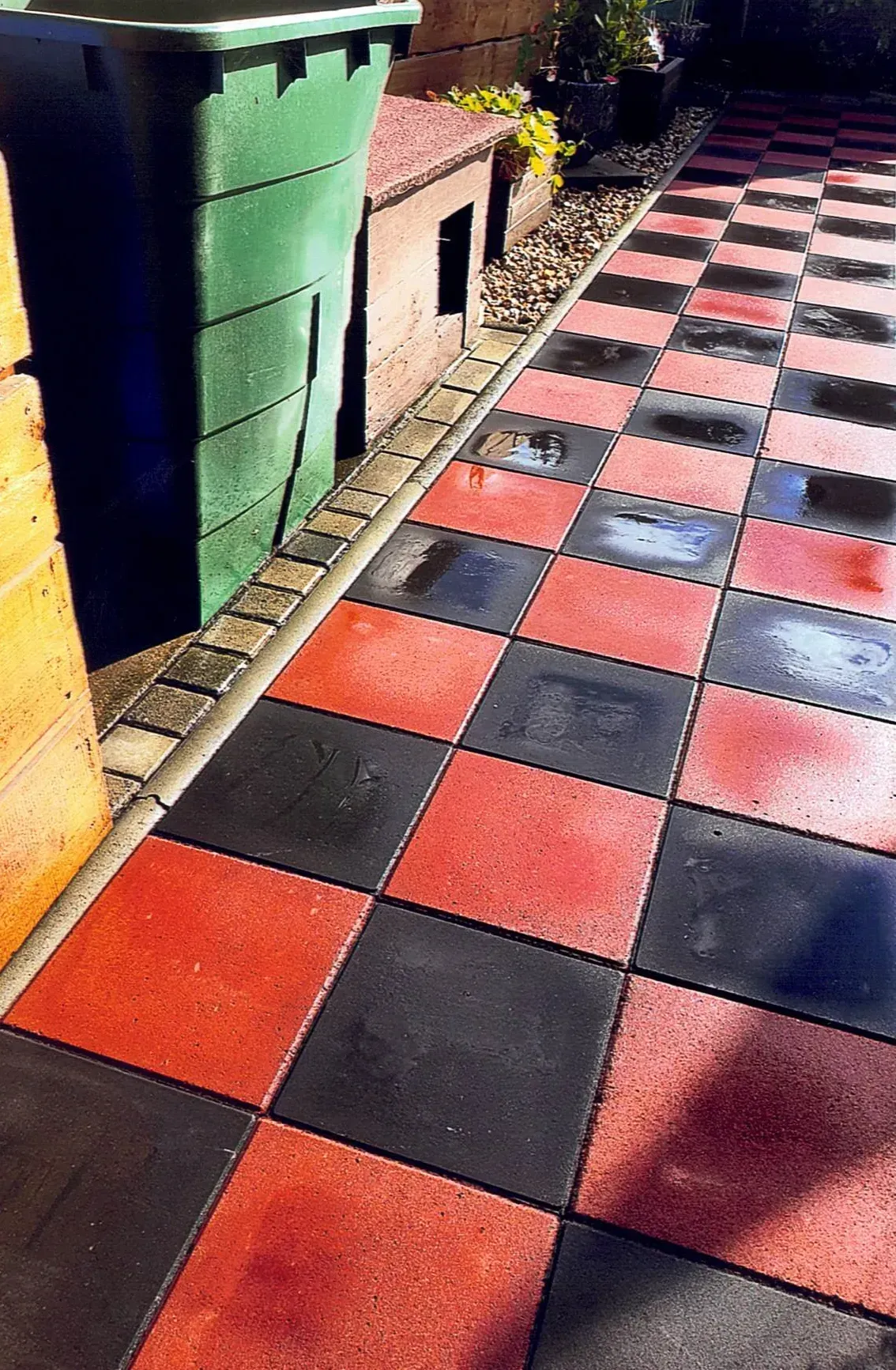 Ein rot-schwarz karierter Boden mit einem grünen Mülleimer im Hintergrund.