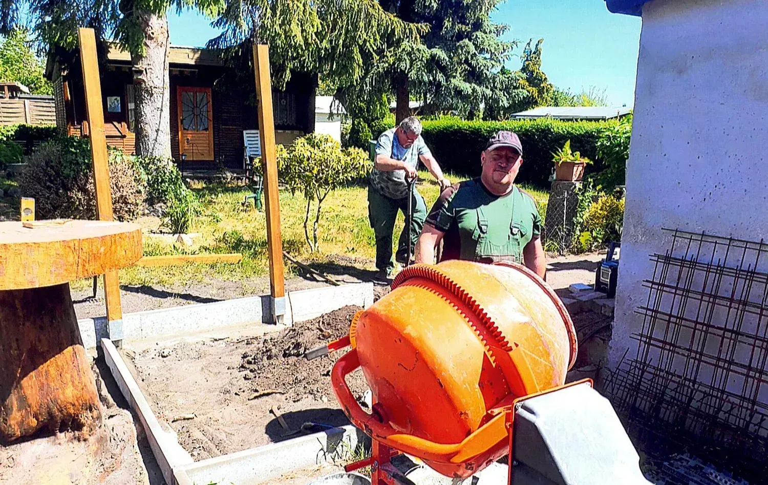 Zwei Männer arbeiten in einem Garten an einem Betonmischer.