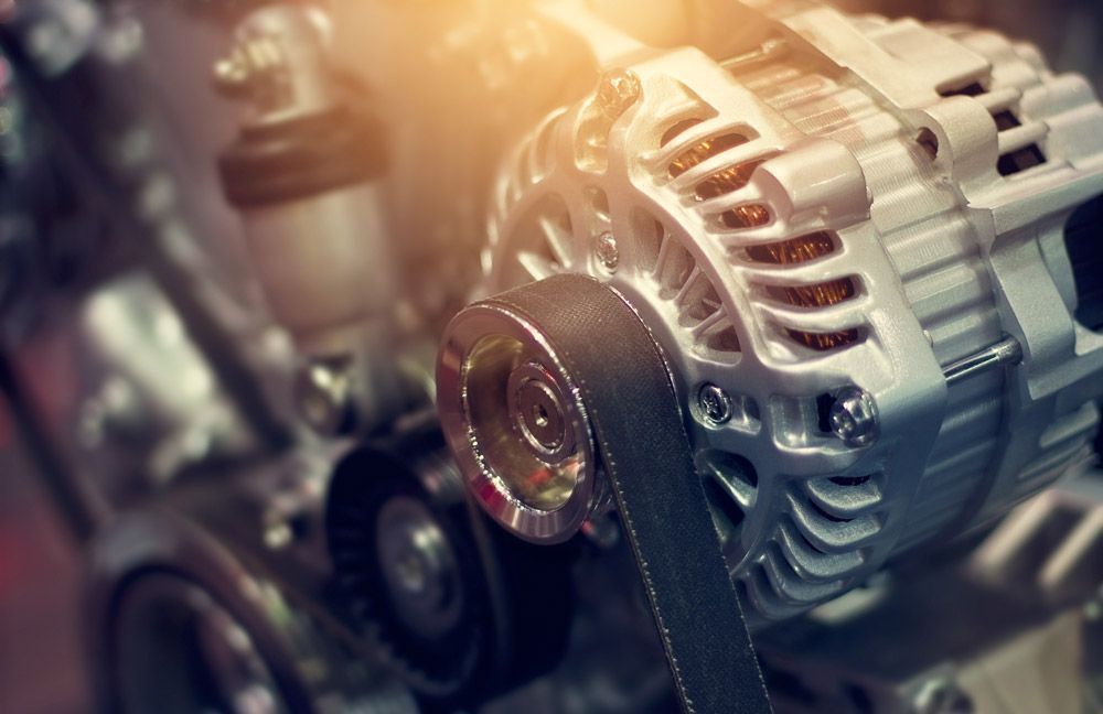 Primer plano de un alternador de motor con correa y poleas en un taller.