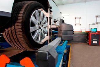 Una rueda de coche en un elevador en un taller de reparación de automóviles, con herramientas y equipos cerca.
