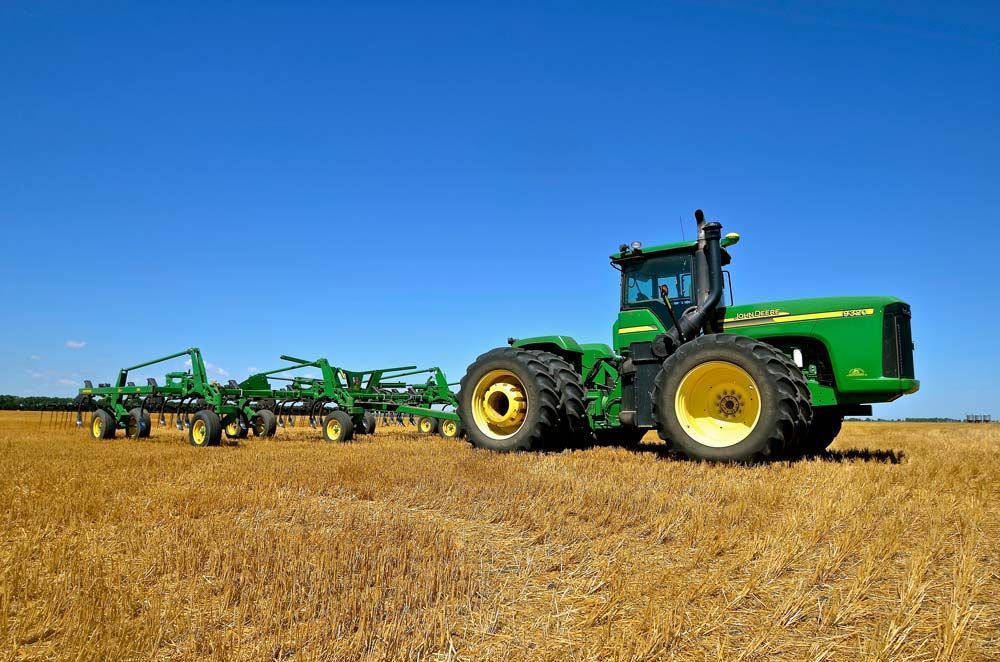 Tractores verdes arando un campo seco bajo un cielo azul despejado.