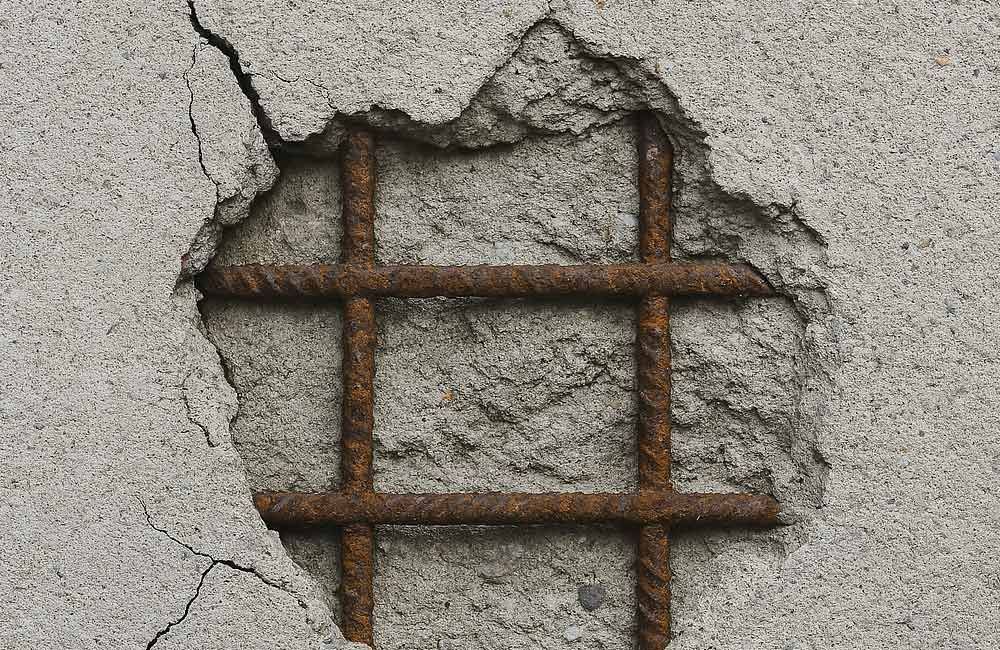 Beschädigte Betonwand, die verrostete Bewehrungsstäbe freilegt.