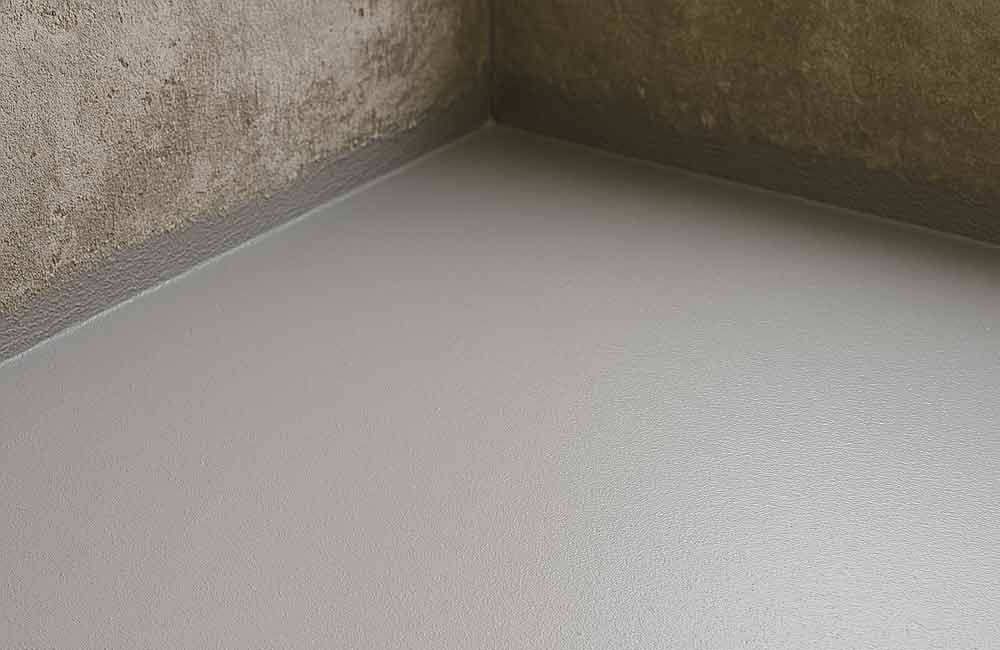 Grauer, glatter Betonboden in einer Ecke, mit einer dunkelgrauen Kante, wo der Boden auf die Wände trifft.