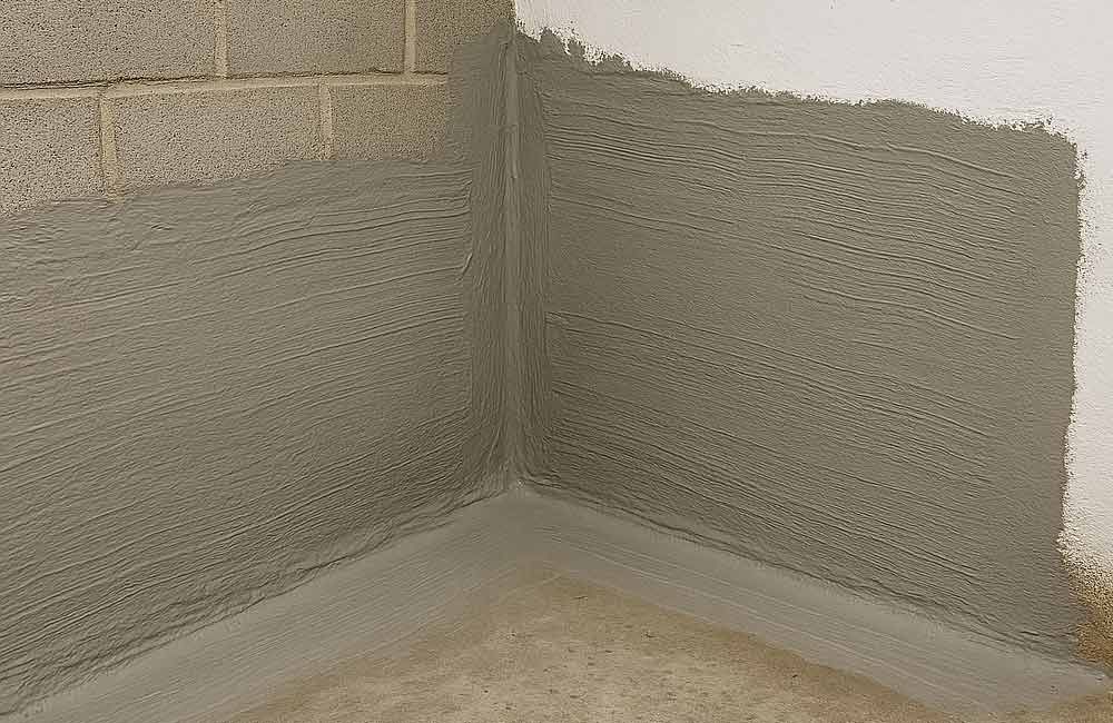 Graues Dichtmittel wurde an der Ecke einer Kellerwand aus Betonsteinen aufgetragen.