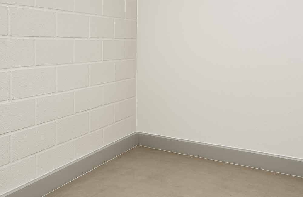 Ecke eines Raumes mit einer weißen Blockwand, einer schlichten weißen Wand und einer grauen Fußleiste entlang eines Betonbodens.