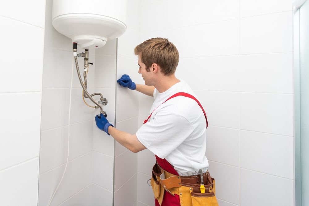 Un hombre está arreglando un calentador de agua en un baño.