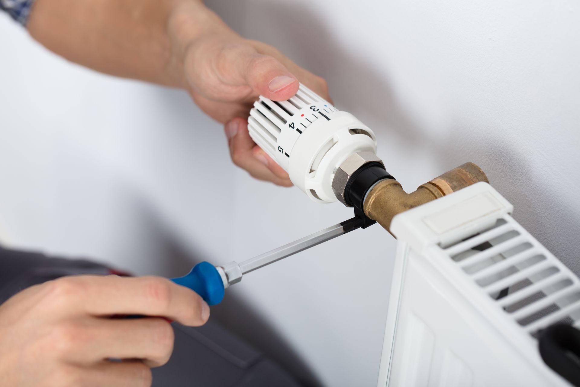 Gros plan sur un plombier-chauffagiste qui fixe un thermostat sur un radiateur à l'aide d'un tournevis.